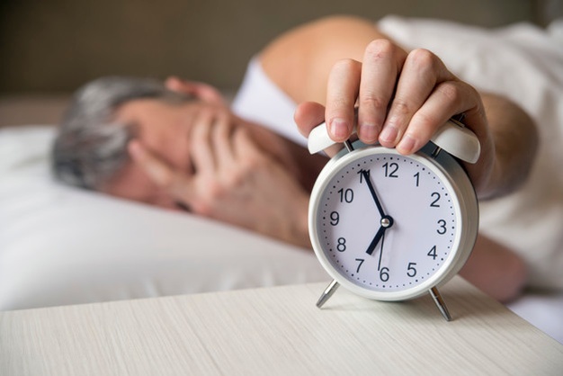 man-lying-bed-turning-off-alarm-clock
